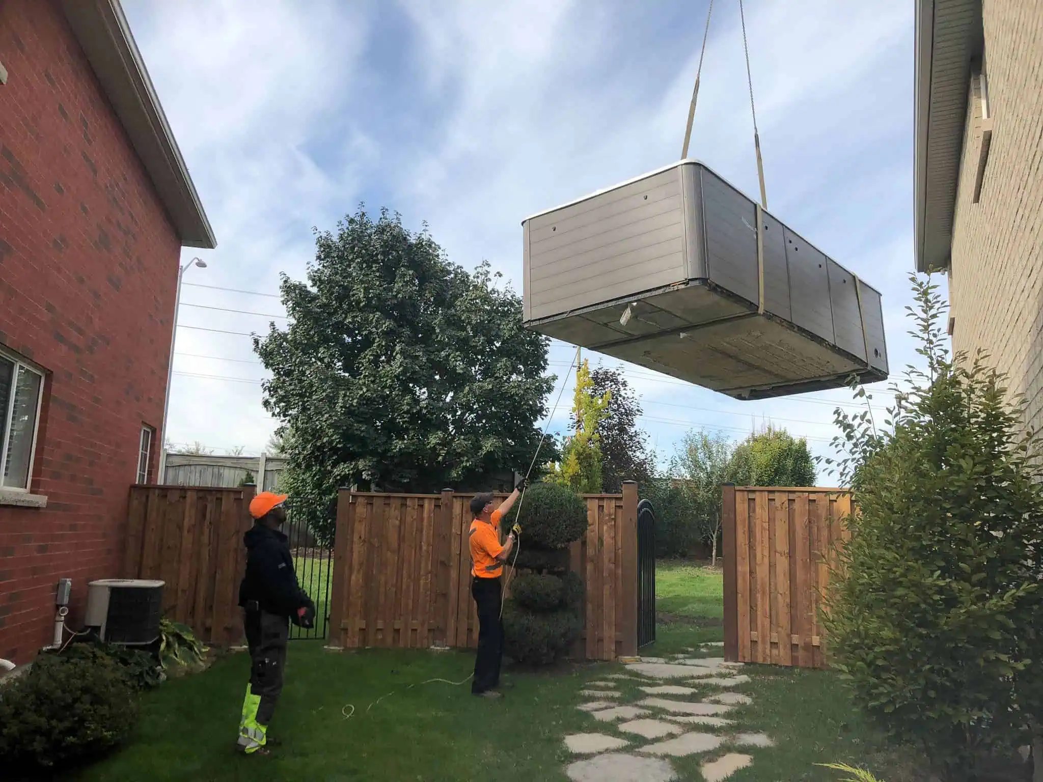 Guiding a swim spa into a backyard with a crane in Caledon.