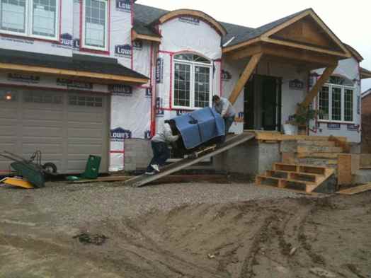 Piano movers pushing an upright piano up a ramp and into a house.