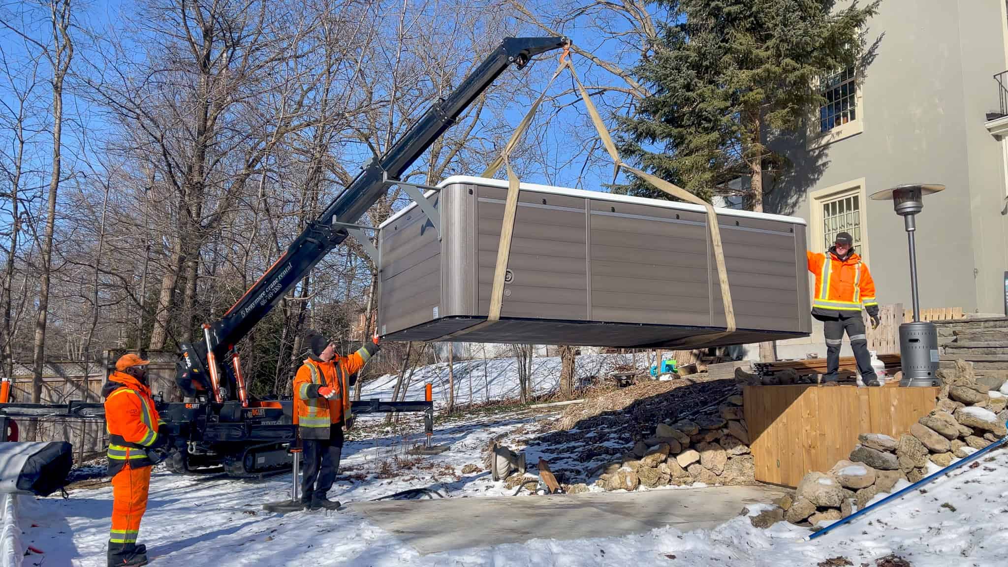 Spider crane placing swim spa on a concrete pad in a backyard.