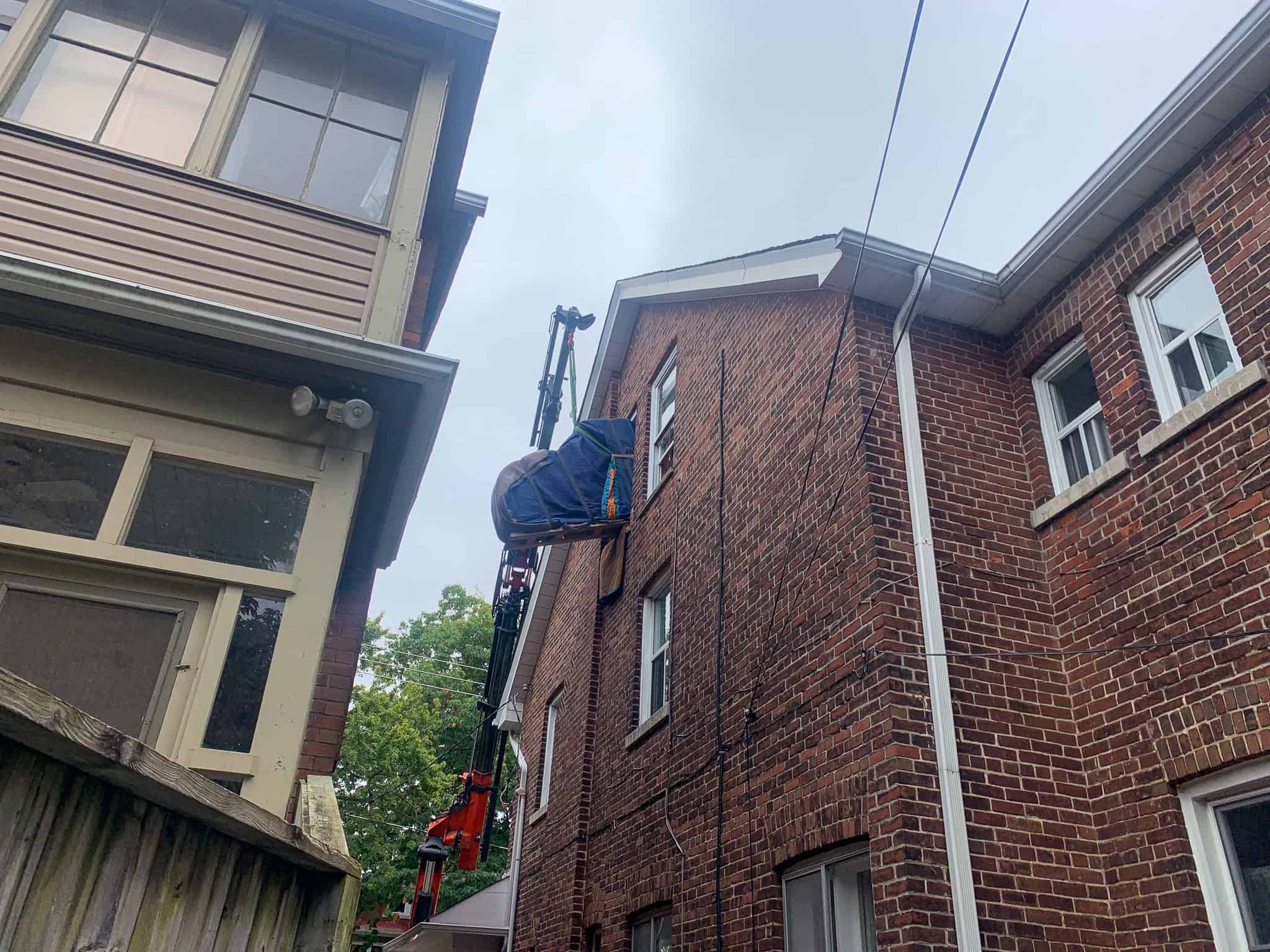 Craning a grand piano in through a window on the third floor of a house.