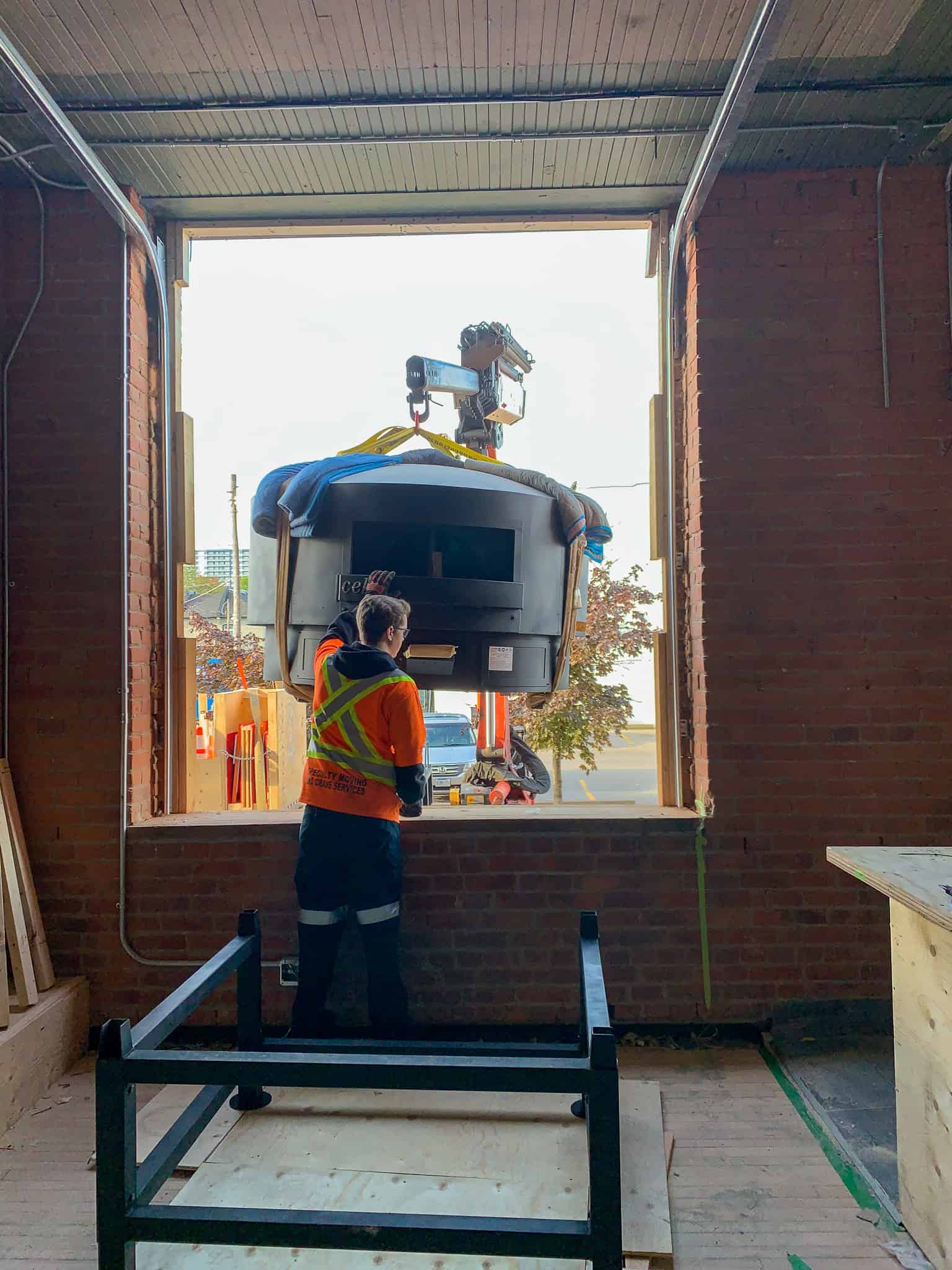 Knuckle crane lifting large pizza oven through large window opening in Hamilton.