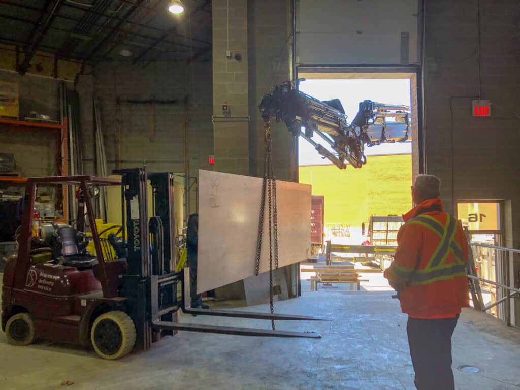 Using a combination of forklift and crane to lift large metal sheets of steel.