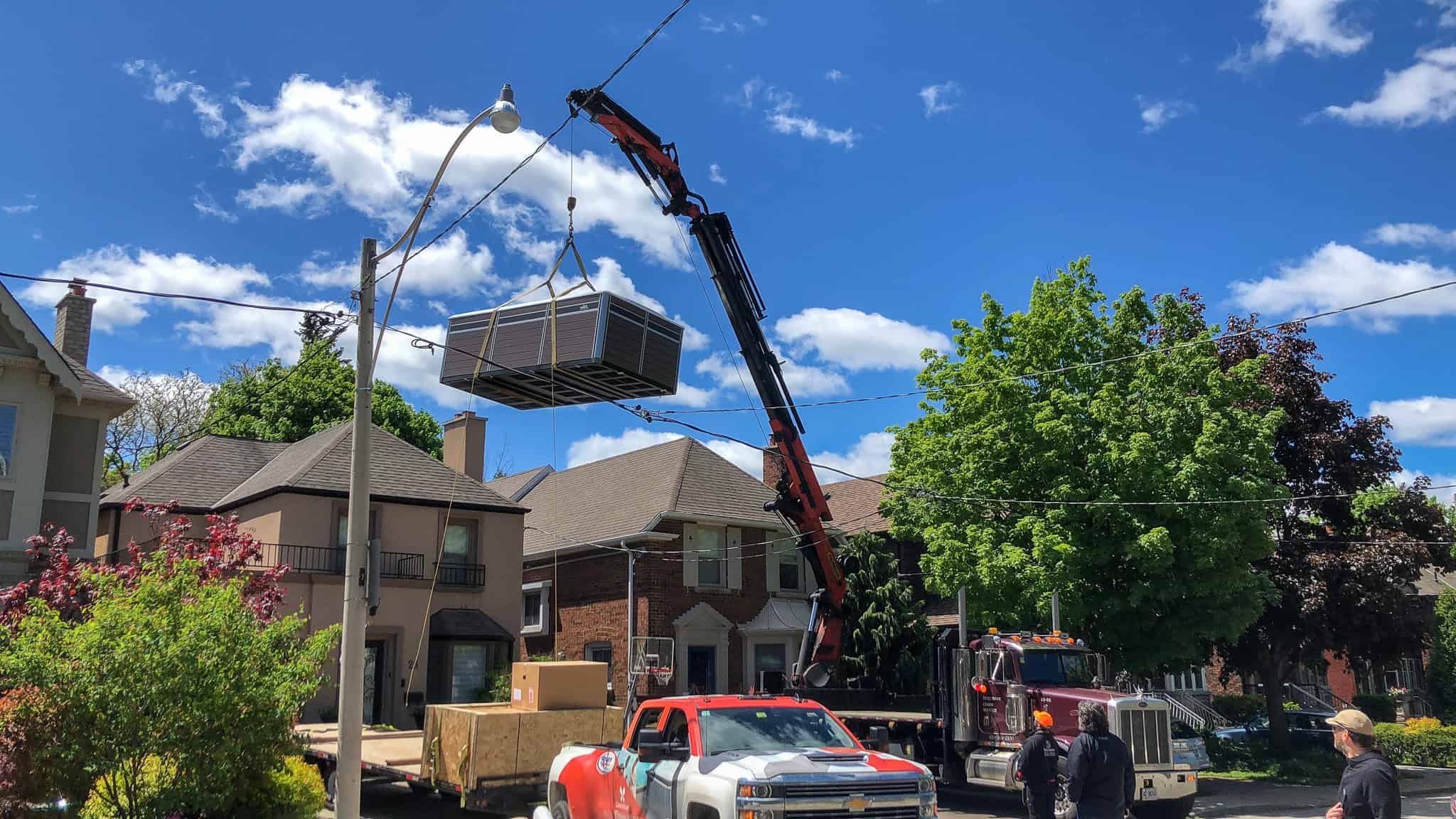 Knuckle crane lifting a large swim spa over a house.