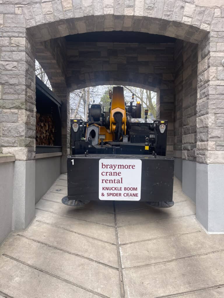 Spider crane driving under an arch in a driveway.