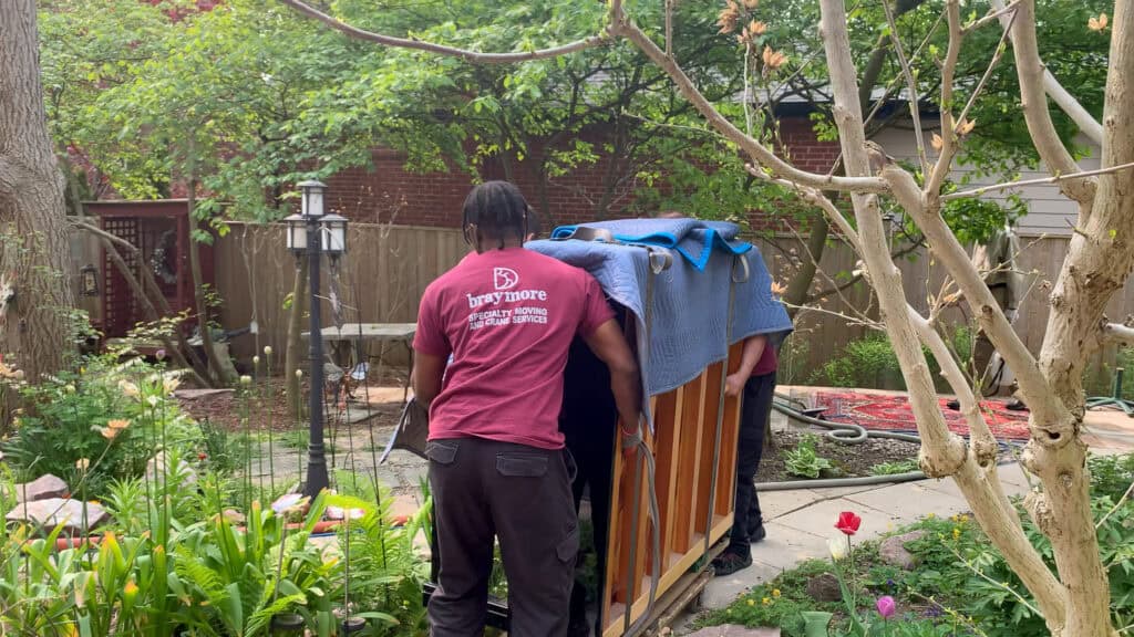 Piano movers rolling an upright piano through a backyard.