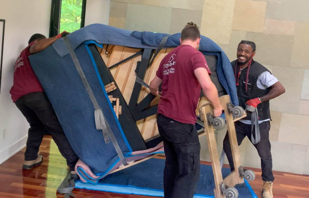 Piano movers tipping a grand piano to place a piano dolly under it.