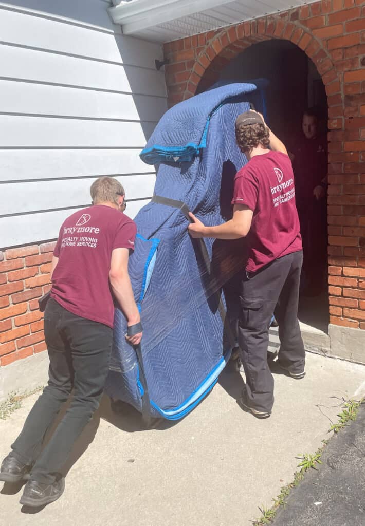 Lifting grand piano up one step and into doorway of house.