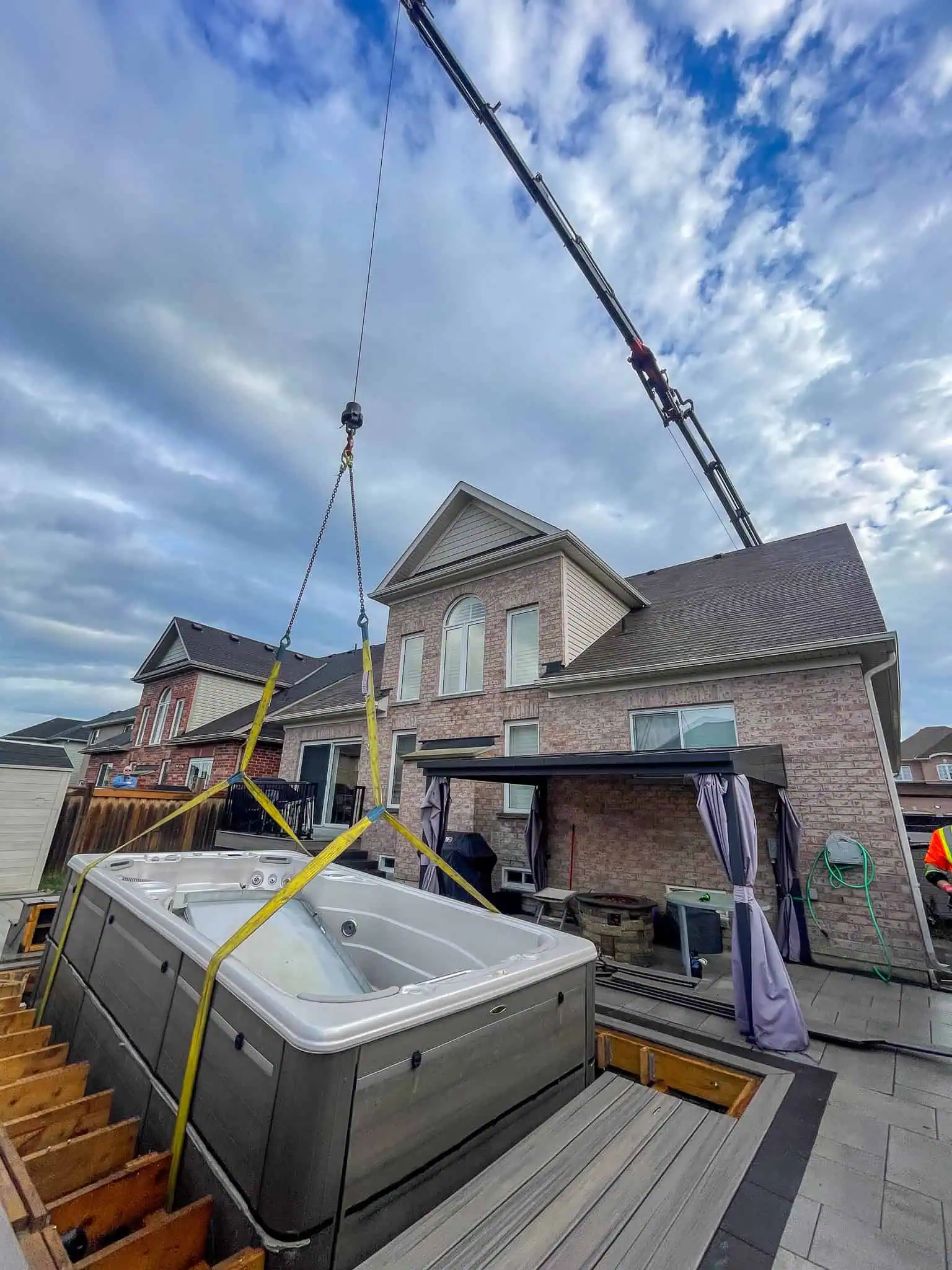 Knuckle crane lifting a swim spa into a backyard deck.
