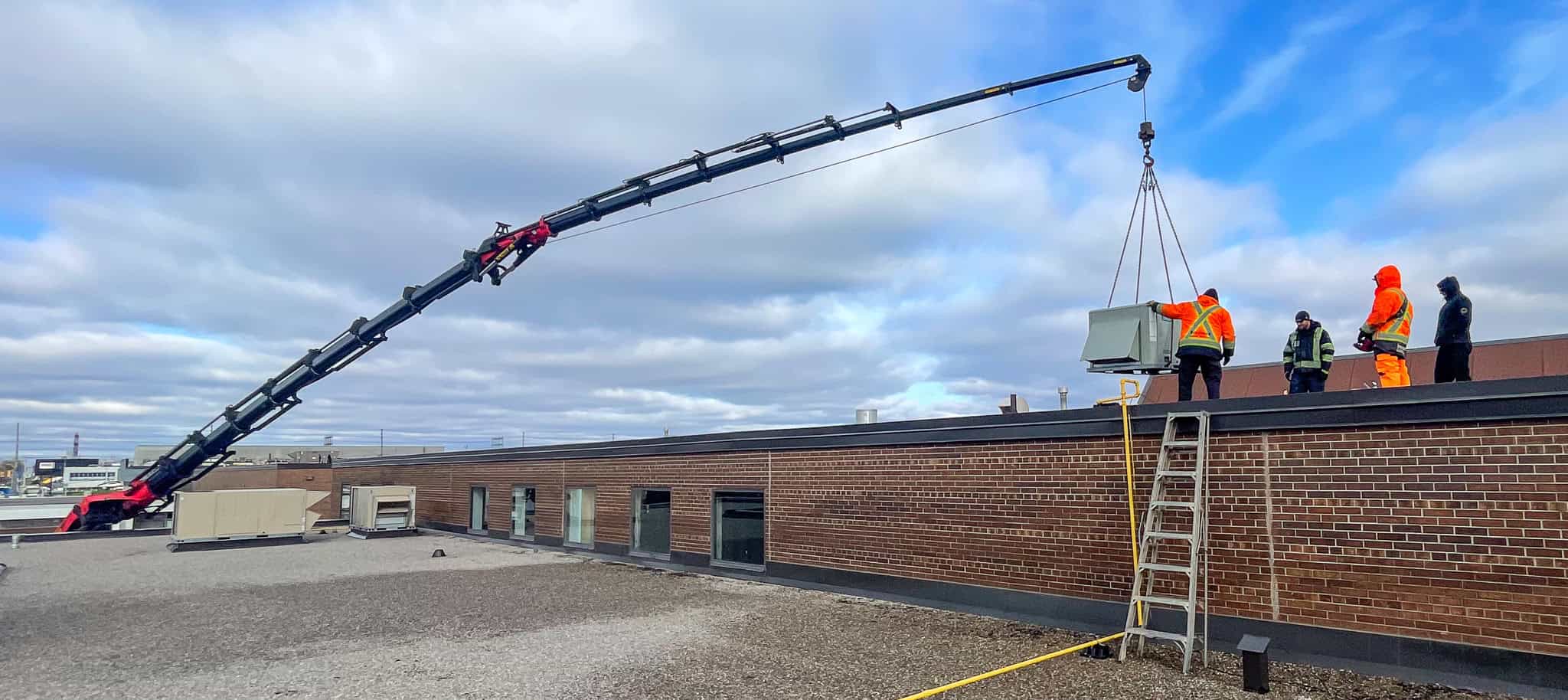 Palfinger PK135002 knuckle crane placing HVAC unit on a commercial building.