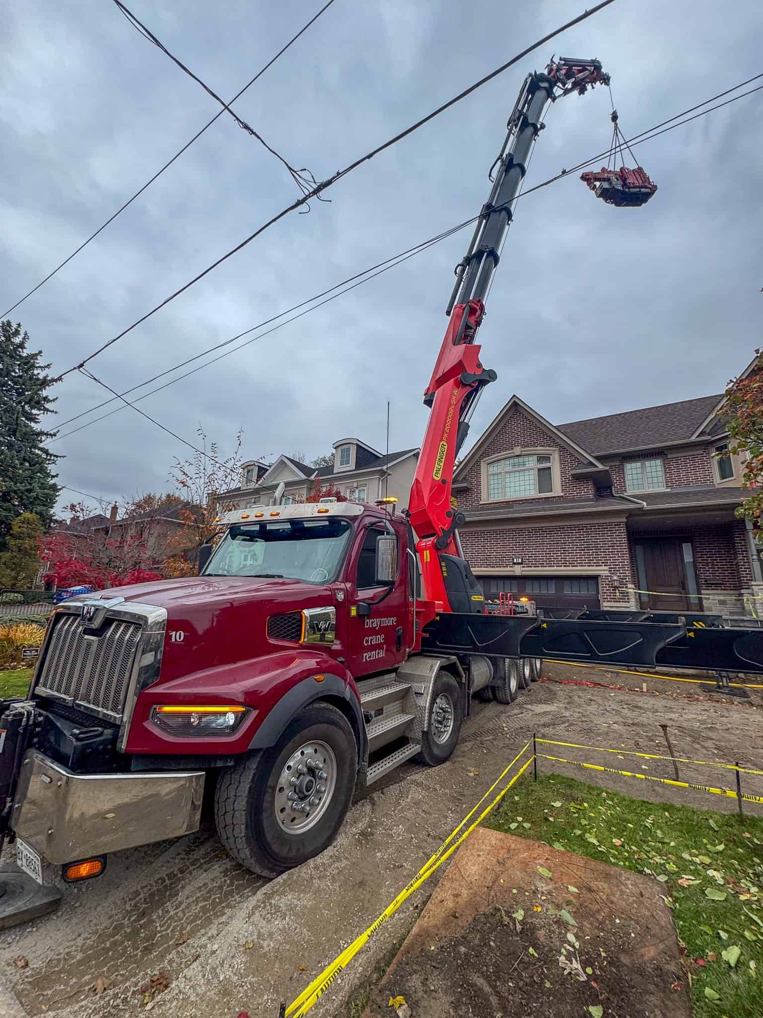 Large knuckle crane lifting a small mini crane into a backyard to lift the extra distance.