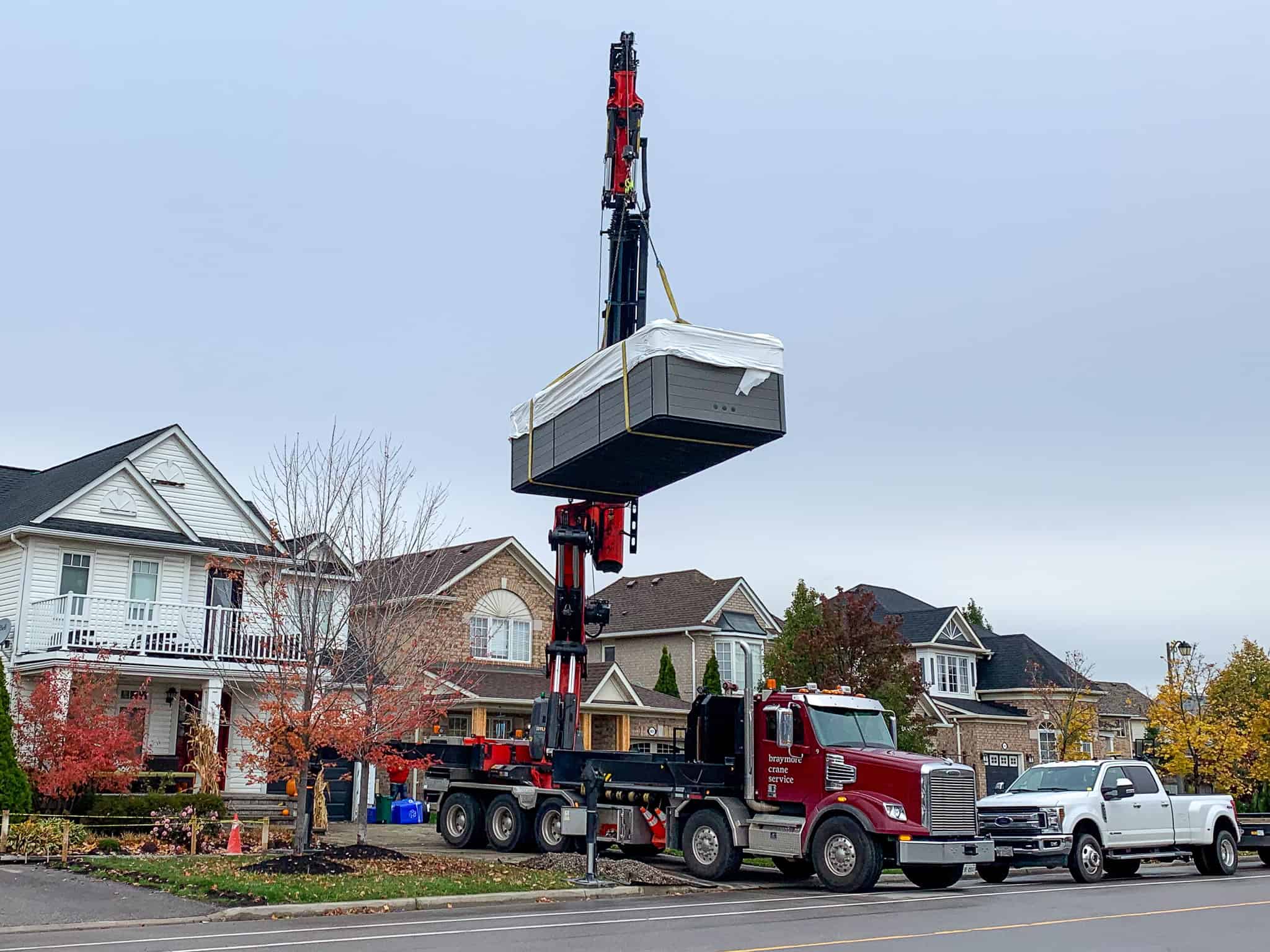 Knuckle crane lifting a large swim spa over a house in Milton, Ontario.