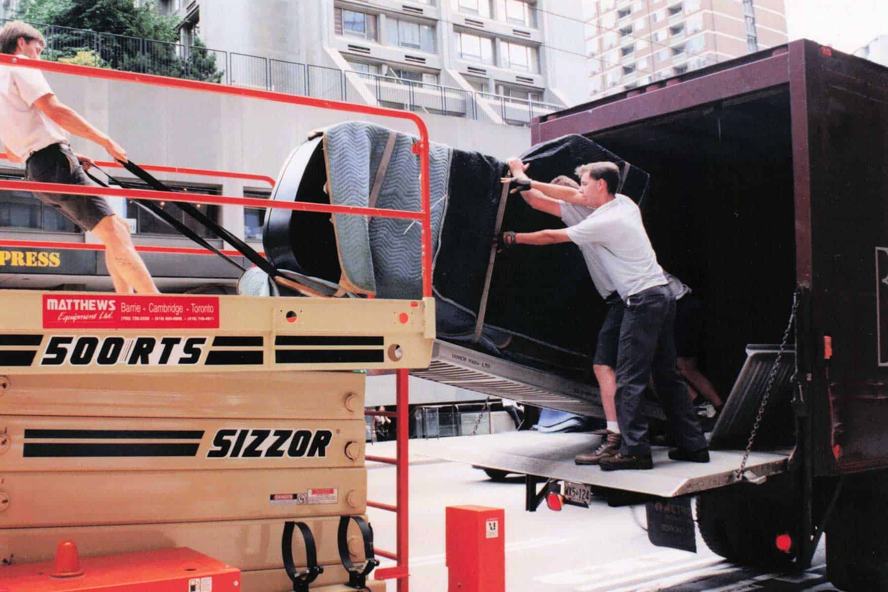 Braymore employees transferring a grand piano from a scissor lift to a truck