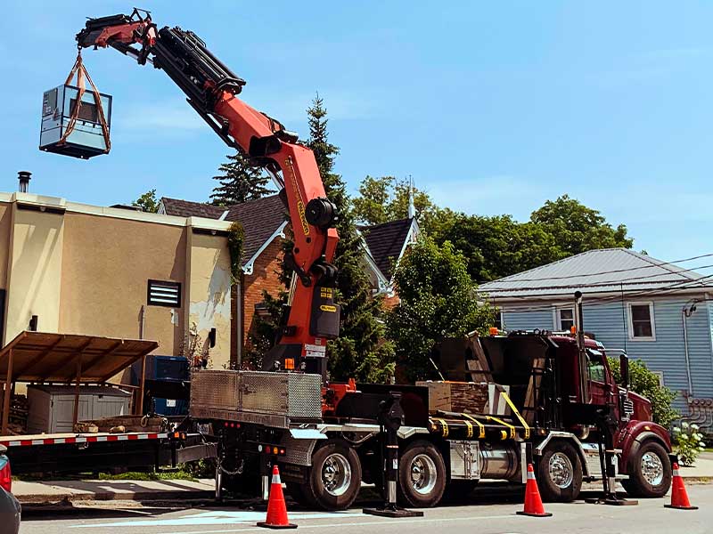 A knuckle crane lifting an air conditioning unit onto a roof