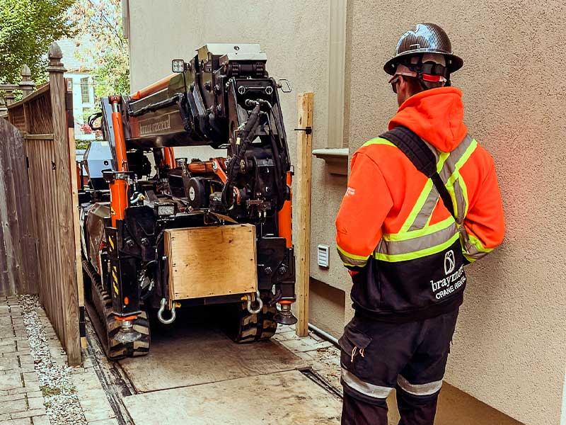A mini crane navigating a tight path through a gate into a backyard.