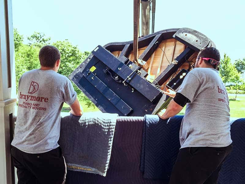 Employees guiding a grand piano as it is craned to a balcony entrance