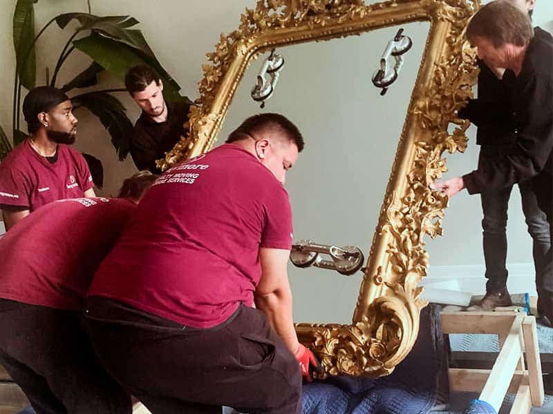 Employees moving a large ornate mirror safely out of its custom-made carrier