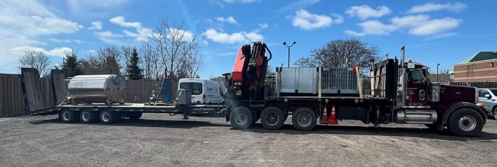 Crane and trailer transporting a large vat and chiller.