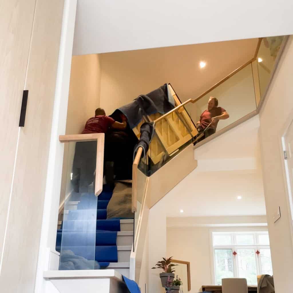Moving an upright piano up a flight of stairs with a tight turn and a glass railing.