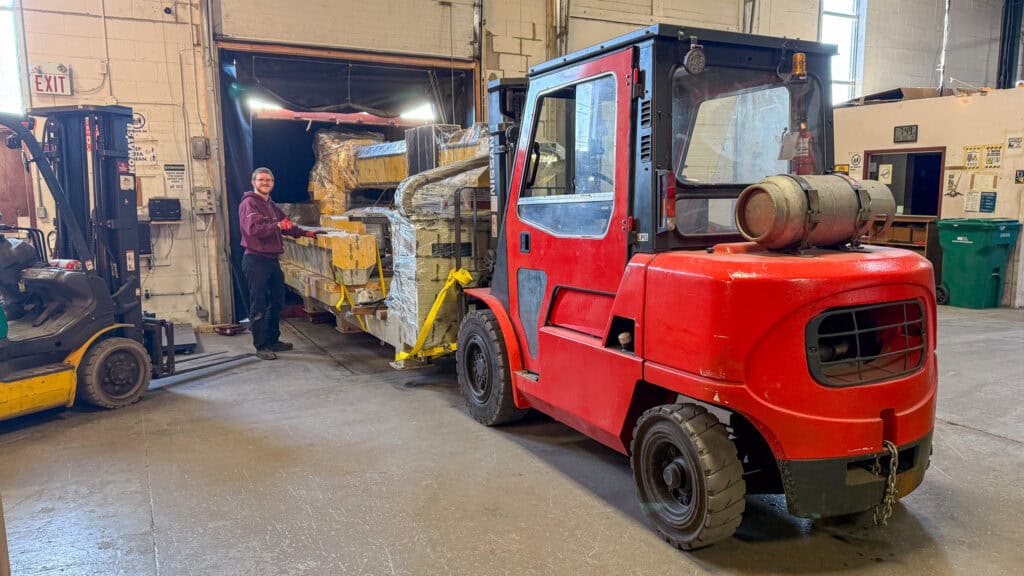 Using a forklift to offload a large piece of machinery off a container.