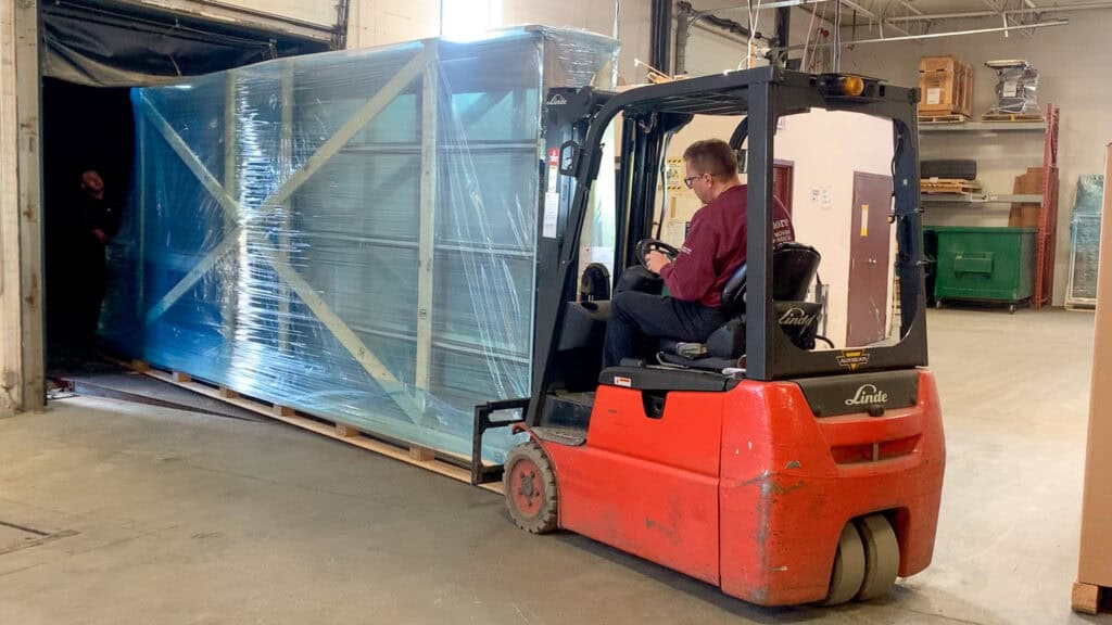Using a forklift to drag a large skid of glass off a container.