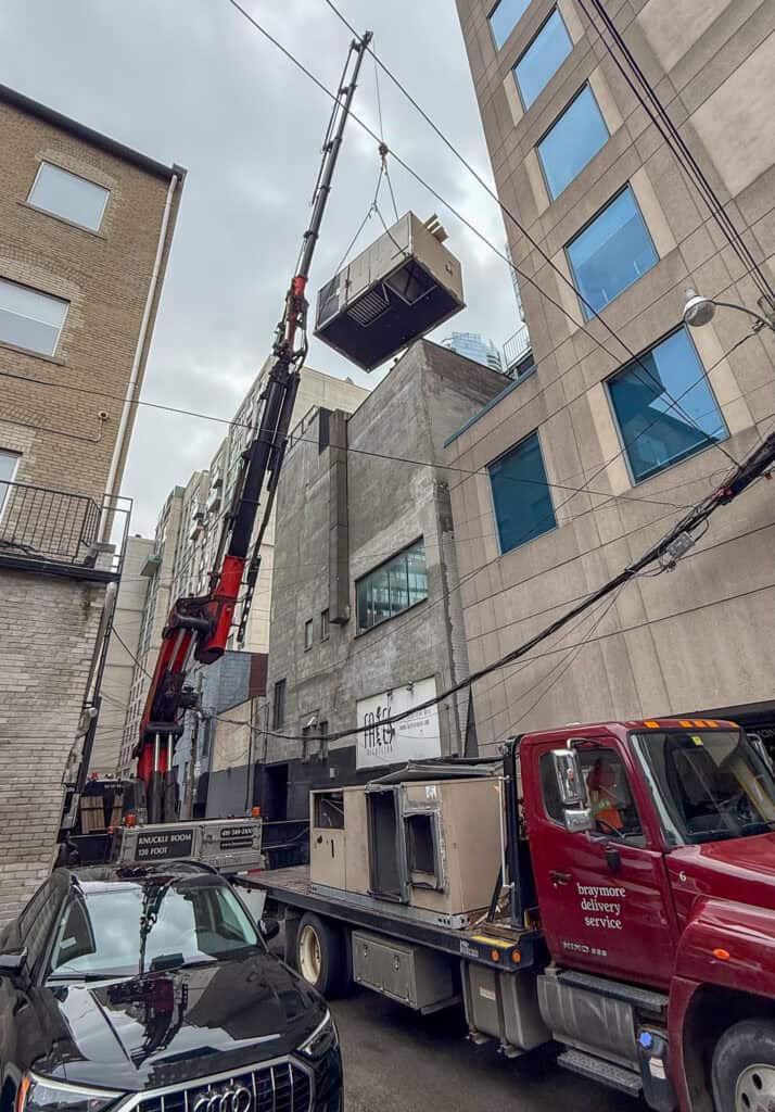 We are using a knuckle crane to lift an HVAC unit off a roof in a tight downtown Toronto laneway onto a flatbed truck.