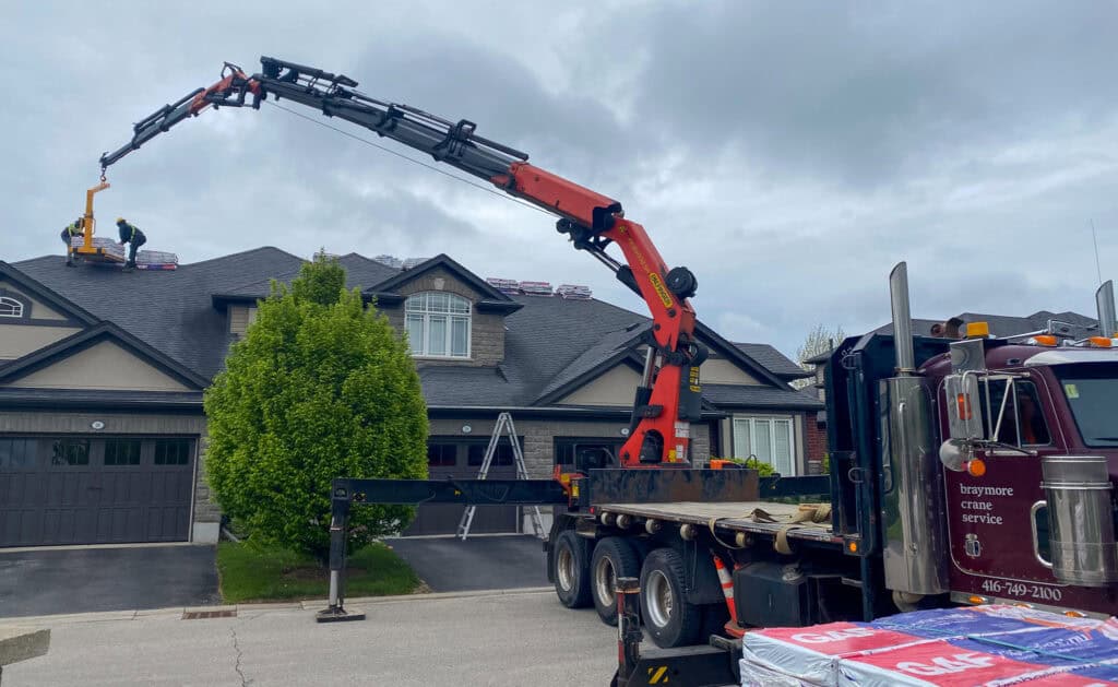We are using a forklift attachment on a crane to lift skids of roofing shingles onto the roof for workers.
